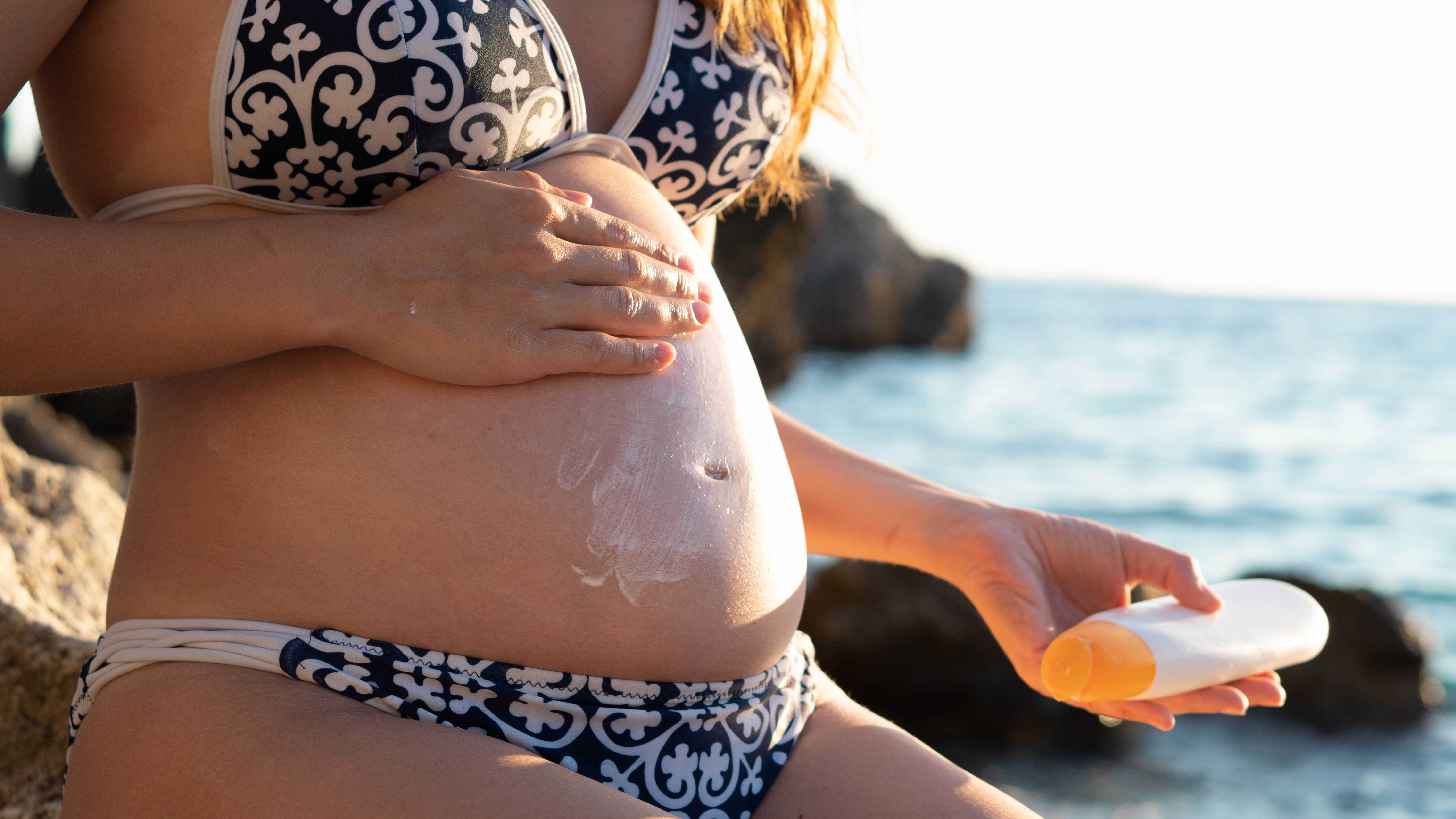 Pregnant woman in bikini outdoors applying sunscreen on her body